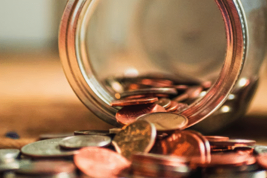 A glass jar tipped over with coins spilling out onto a surface.