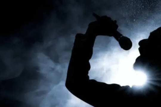 Silhouette of a singer passionately performing with a microphone under dramatic lighting and smoke.