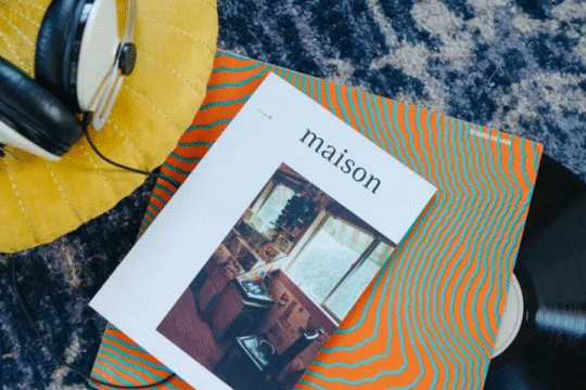 Overhead view of a vinyl record, headphones, and a "maison" magazine on a colorful surface.