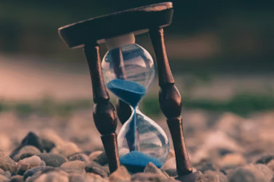 Close-up of a vintage hourglass with blue sand placed on pebbles, symbolizing the passage of time.