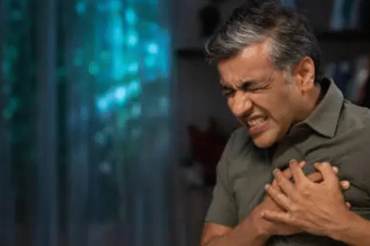 Middle-aged man clutching his chest in pain, showing symptoms of a heart attack indoors.