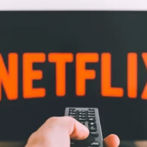 Hand holding remote control in front of TV displaying Netflix logo.
