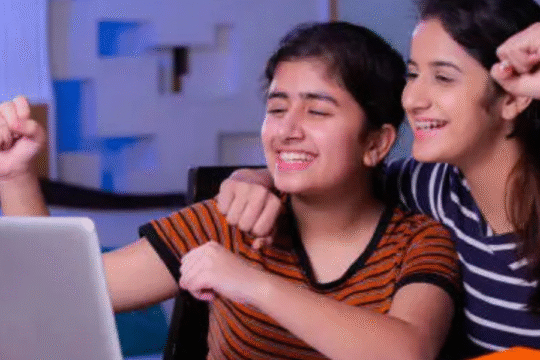 Two happy teenage girls celebrating while looking at a laptop.