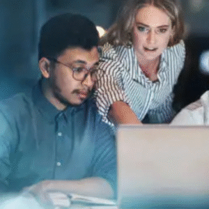 Three professionals working late at night, focused on laptop screen.