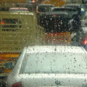 Traffic congestion in Indian city during heavy monsoon rain, viewed through a rain-soaked windshield.