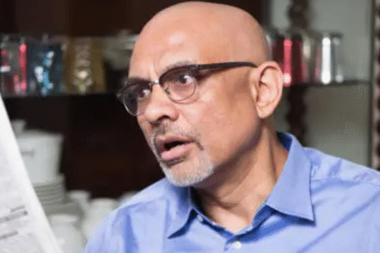 Surprised elderly man in glasses reading a newspaper at home.