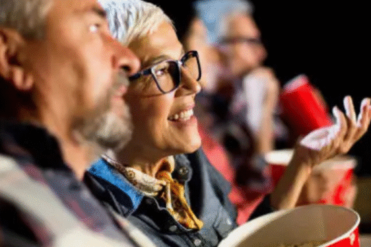 Smiling elderly couple enjoying a movie with popcorn in a cinema.