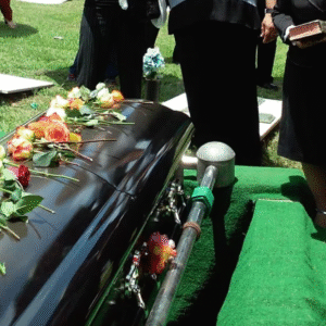 Casket adorned with flowers during a funeral ceremony with mourners in black.