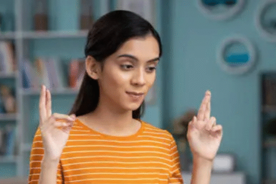 Young Indian woman crossing fingers with hopeful expression during online result check at home.