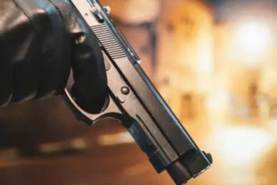 Close-up of a person holding a handgun with gloves in a dimly lit urban alley.