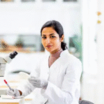 Female scientist in lab coat working with a microscope in a bright laboratory.