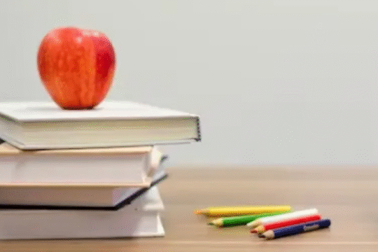 Stack of books with a red apple on top, colorful pencils, and ABC blocks on a wooden table.
