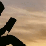 Silhouette of a child reading a book under a tree during sunset
