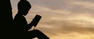 Silhouette of a child reading a book under a tree during sunset