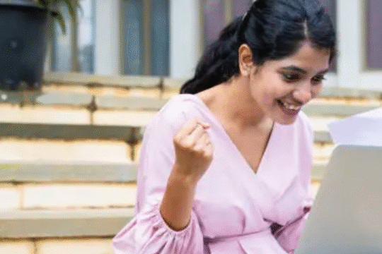 Excited young woman checks her results online on a laptop while sitting on outdoor steps