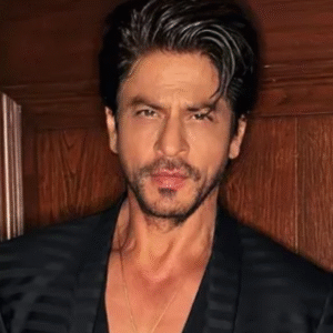 Man in a black striped blazer posing against a wooden wall.