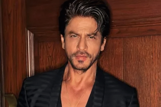 Man in a black striped blazer posing against a wooden wall.