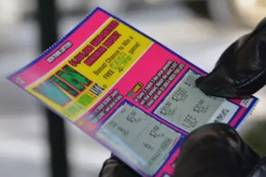 Person wearing black gloves holding a colorful lottery scratch card with visible winning amounts.