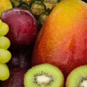 Close-up of assorted fresh fruits including green grapes, mango, kiwi, apple, plum, and pineapple.