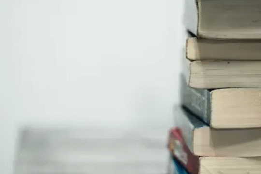 Stack of old, slightly worn books piled vertically against a plain white background.
