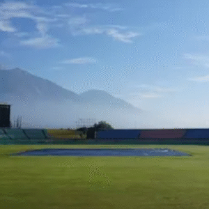 Scenic view of an empty cricket stadium with snow-capped mountains in the background under a clear blue sky.