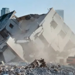 Partially collapsed multi-storey building surrounded by dust and debris