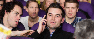 Man talking on phone in theater while others look annoyed
