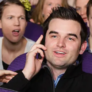 Man talking on phone in theater while others look annoyed