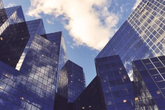 Modern high-rise glass office buildings reflecting the sky and clouds in a cityscape.