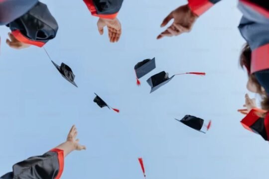 Graduates in black and red gowns celebrating by tossing caps into the sky.