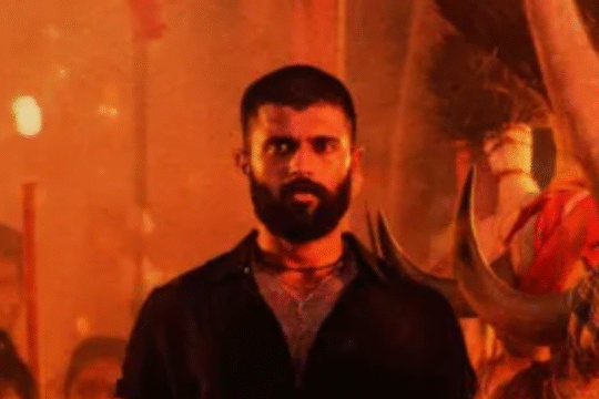 Actor Vijay Deverakonda stands shirtless in a scene with a stylized yellow and red background.