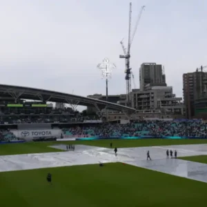 A cricket stadium with the pitch covered on a cloudy day.