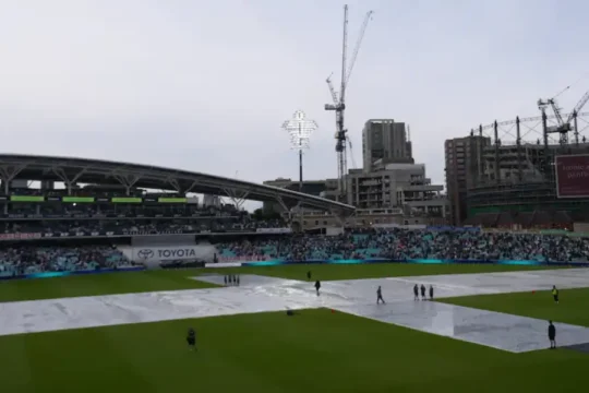A cricket stadium with the pitch covered on a cloudy day.