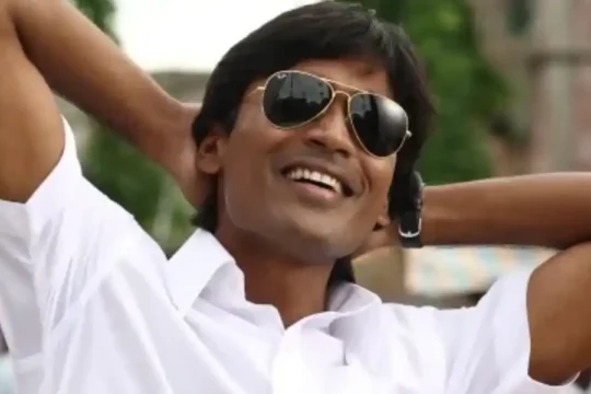 Indian actor Dhanush smiling with hands behind his head.