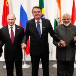 Leaders of the BRICS nations, including Xi Jinping, Vladimir Putin, Jair Bolsonaro, Narendra Modi, and Cyril Ramaphosa, holding hands.