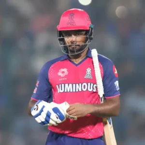 Indian cricketer Sanju Samson in a pink and blue Rajasthan Royals jersey, holding a bat.